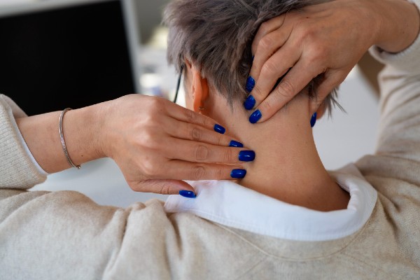 Une femme se masse la nuque endolorie pour tenter de soulager sa douleur.